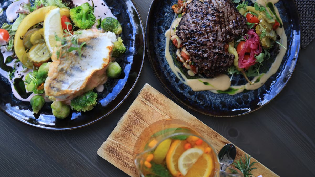 Top view of gourmet fish and steak dishes with fresh citrus and herbs on a stylish table setting.